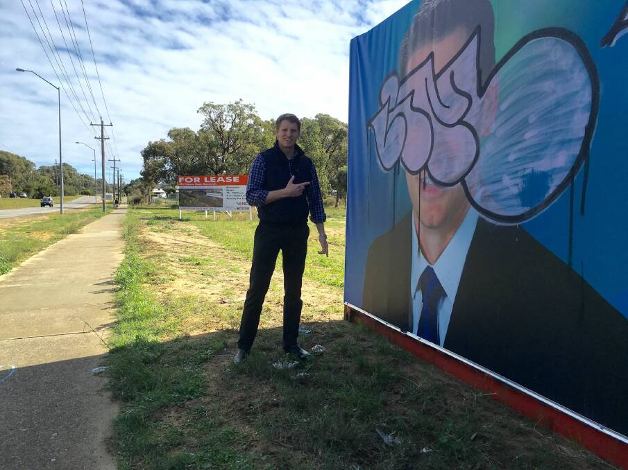 Not quite art: Canning MP Andrew Hastie with the campaign poster on Pinjarra Road that copped a spray from a vandal over the weekend. Photo: Facebook.