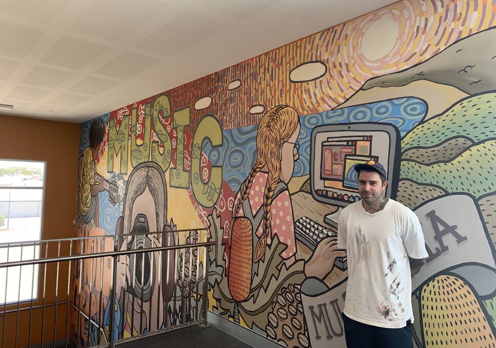 Local artist Ricky Gibson with a mural he created at Coastal Lakes College. Photo: Supplied.